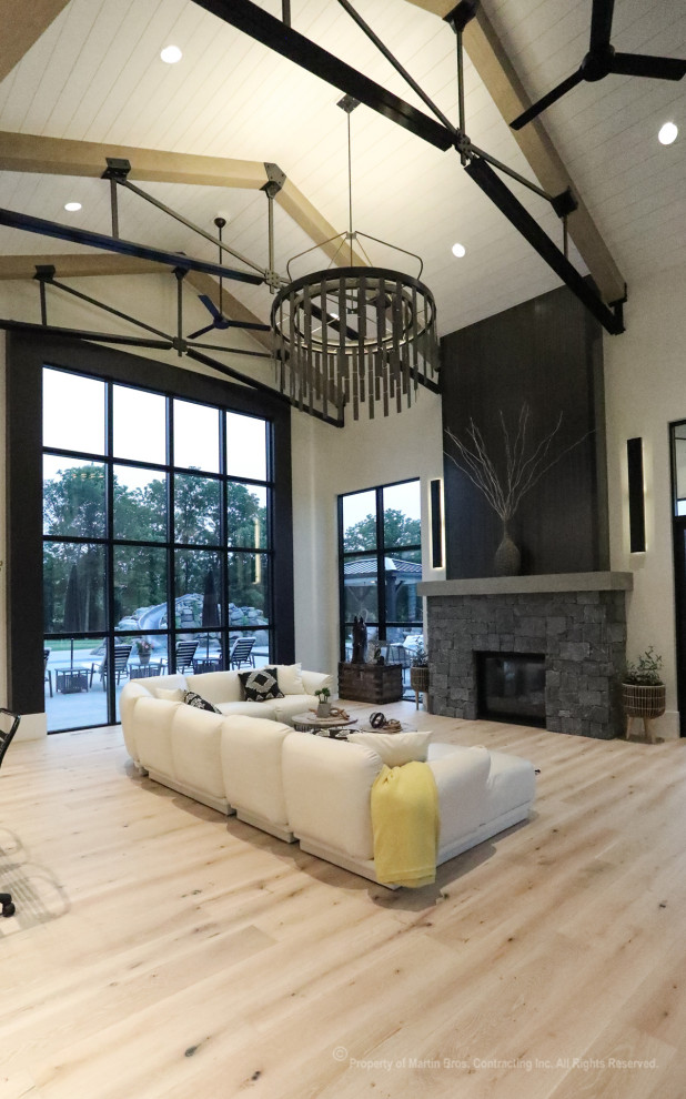 Photo of an expansive industrial open concept living room in Other with white walls, light hardwood floors, a two-sided fireplace, no tv and vaulted.