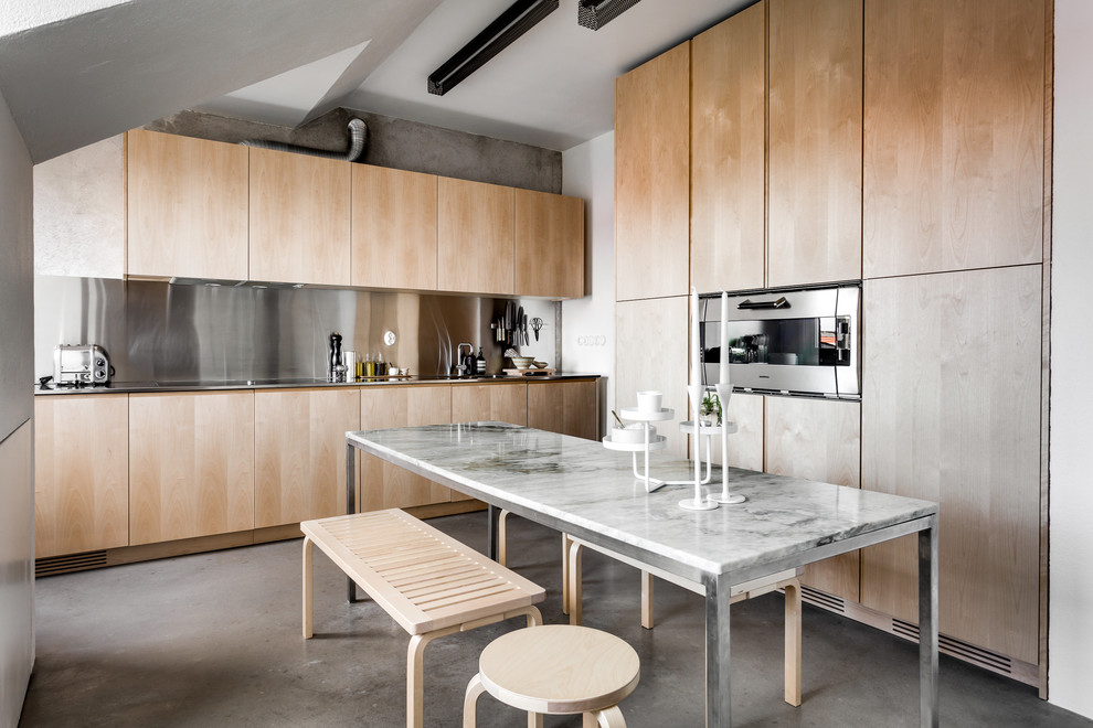 This is an example of a large contemporary eat-in kitchen in Stockholm with concrete floors, flat-panel cabinets, light wood cabinets and metallic splashback.