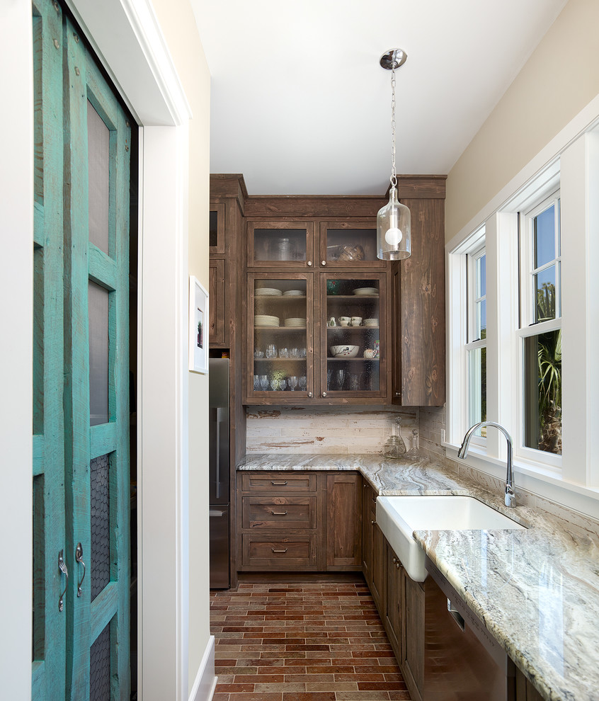 Design ideas for an eclectic galley separate kitchen in Charleston with a farmhouse sink, glass-front cabinets, distressed cabinets, quartzite benchtops, white splashback, ceramic splashback, stainless steel appliances and brick floors.