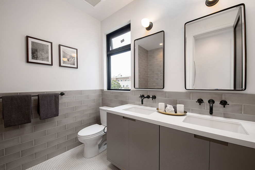 This is an example of a mid-sized transitional kids bathroom in San Francisco with flat-panel cabinets, grey cabinets, a one-piece toilet, gray tile, glass sheet wall, white walls, ceramic floors, an undermount sink and engineered quartz benchtops.