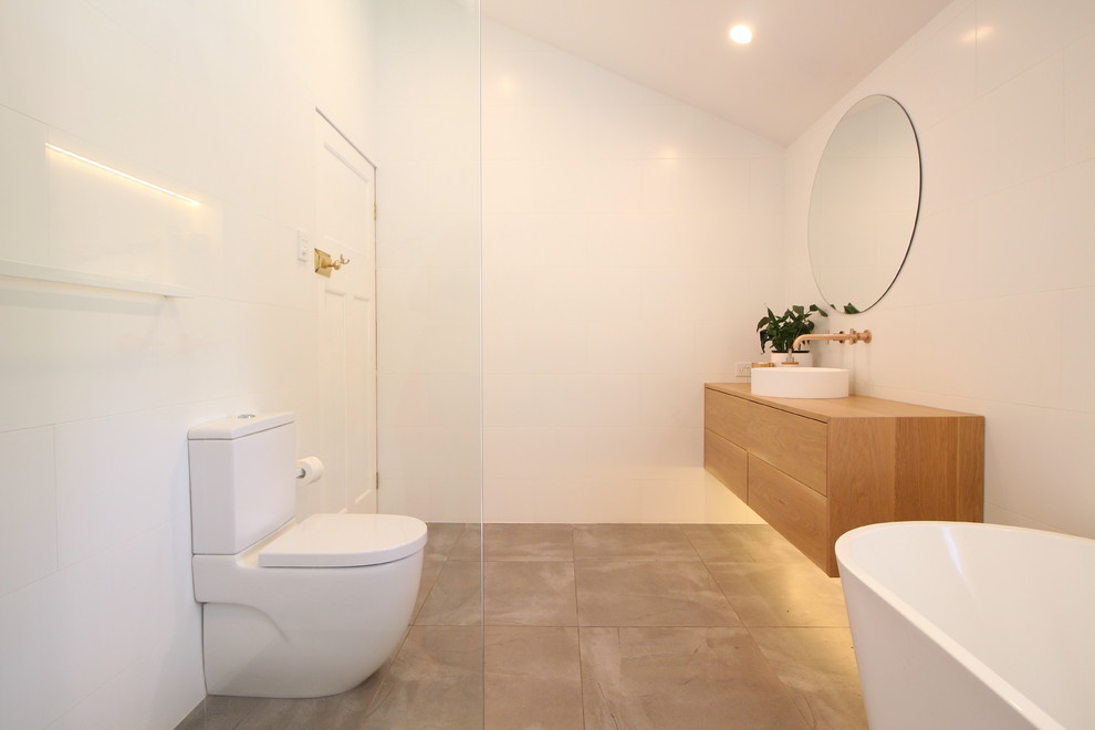 Photo of a contemporary 3/4 bathroom in Brisbane with flat-panel cabinets, medium wood cabinets, a freestanding tub, white tile, white walls, a vessel sink, wood benchtops and grey floor.