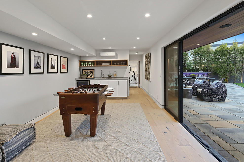 This is an example of a mid-sized modern open concept family room in Los Angeles with a game room, a home bar, grey walls, light hardwood floors, no fireplace, no tv and beige floor.