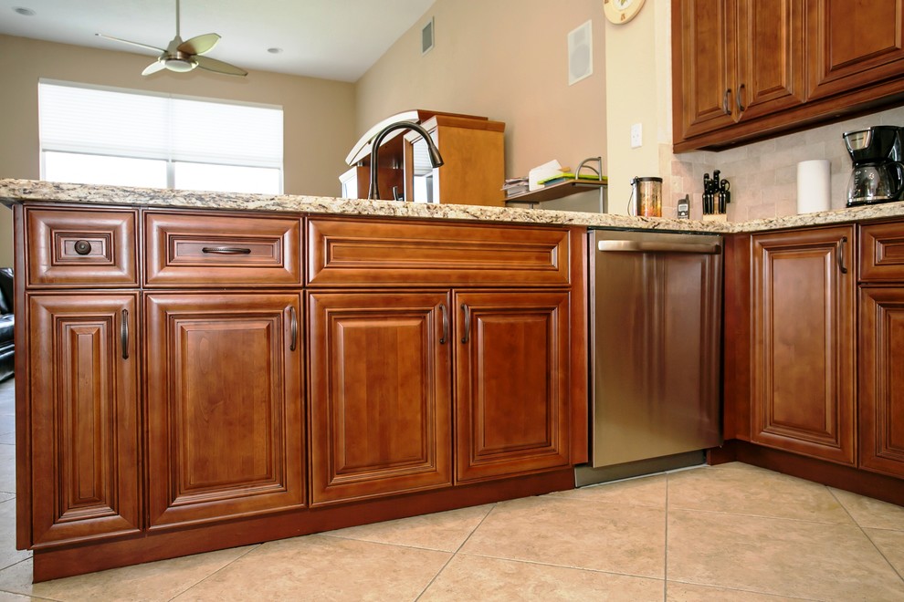 Eat-in kitchen - mid-sized transitional u-shaped porcelain tile eat-in kitchen idea in Miami with an undermount sink, raised-panel cabinets, brown cabinets, granite countertops, beige backsplash, stone tile backsplash, stainless steel appliances, beige walls and a peninsula
