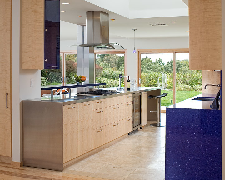 Photo of a mid-sized contemporary galley separate kitchen in San Diego with an undermount sink, flat-panel cabinets, light wood cabinets, stainless steel benchtops, blue splashback, stone slab splashback, stainless steel appliances, porcelain floors, a peninsula, beige floor and blue benchtop.