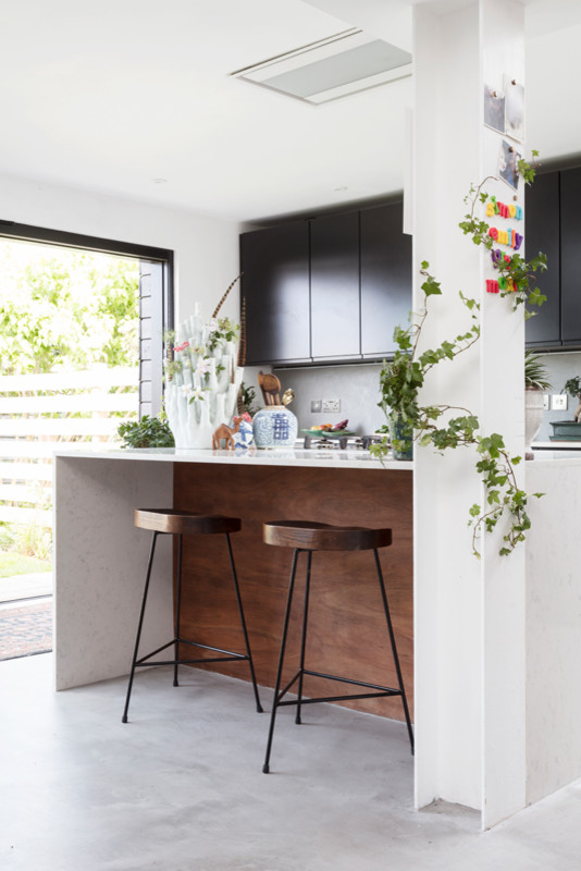 Inspiration for a large eclectic eat-in kitchen in Edinburgh with an integrated sink, flat-panel cabinets, black cabinets, quartzite benchtops, grey splashback, ceramic splashback, panelled appliances, concrete floors, with island, grey floor and white benchtop.