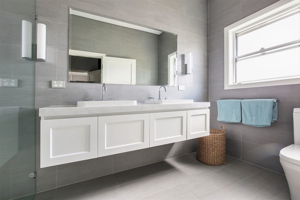 Photo of a large transitional master bathroom in Sydney with shaker cabinets, white cabinets, an alcove shower, a one-piece toilet, gray tile, porcelain tile, grey walls, porcelain floors, a wall-mount sink, engineered quartz benchtops, grey floor, a hinged shower door and multi-coloured benchtops.