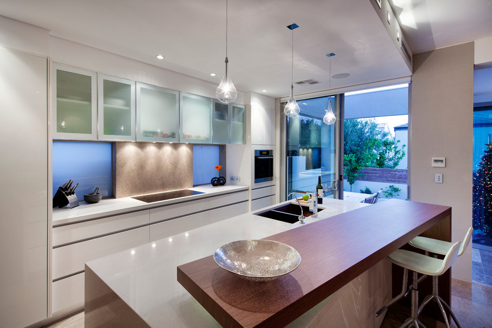 Design ideas for a contemporary eat-in kitchen in Perth with an undermount sink, flat-panel cabinets, white cabinets, wood benchtops, brown splashback, stone slab splashback, stainless steel appliances, travertine floors and with island.