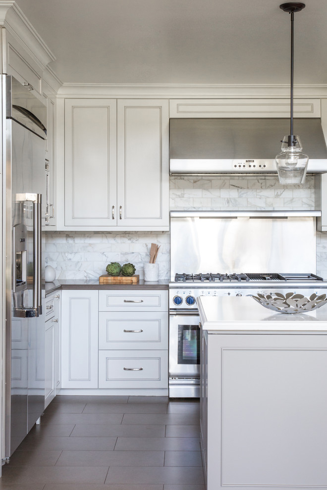 Mid-sized traditional l-shaped open plan kitchen in Los Angeles with recessed-panel cabinets, white cabinets, white splashback, stainless steel appliances, with island, an undermount sink, quartz benchtops, porcelain floors and marble splashback.