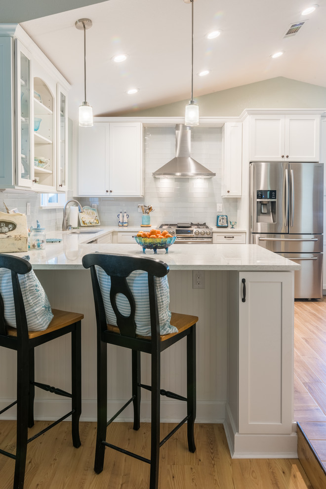 Photo of a mid-sized beach style u-shaped eat-in kitchen in Sacramento with an undermount sink, white cabinets, marble benchtops, white splashback, glass tile splashback, stainless steel appliances, ceramic floors, a peninsula and shaker cabinets.