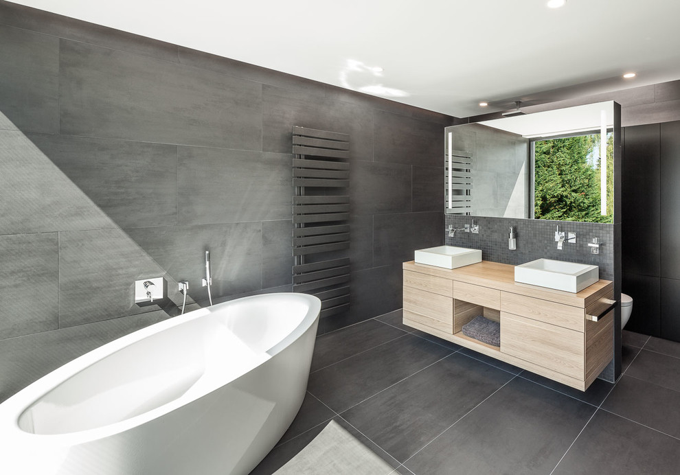 Badezimmer En Suite With Aufsatzwaschbecken, freistehender Badewanne, Wandtoilette, schwarzen Fliesen, schwarzer Wandfarbe, flächenbündigen Schrankfronten, Mosaikfliesen, Waschtisch aus Holz, schwarzen Schränken, bodengleicher Dusche and beiger Waschtischplatte in Cologne