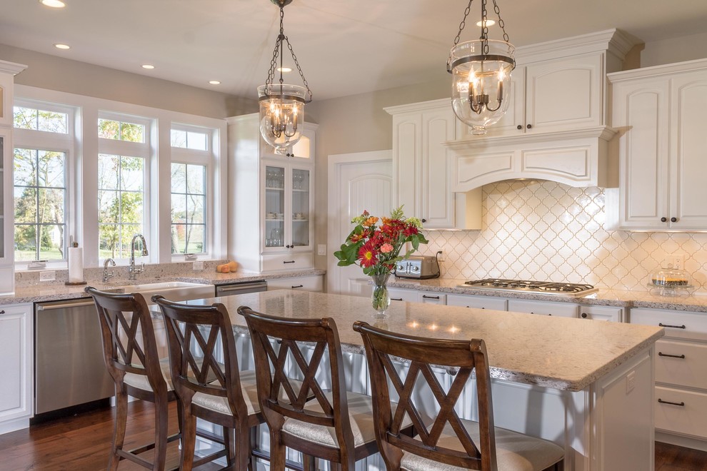This is an example of a traditional kitchen in Other with a farmhouse sink, raised-panel cabinets, white cabinets, white splashback, stainless steel appliances, dark hardwood floors and with island.