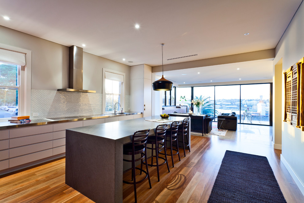 This is an example of a mid-sized single-wall eat-in kitchen in Sydney with an integrated sink, flat-panel cabinets, grey cabinets, ceramic splashback, stainless steel appliances, medium hardwood floors and with island.