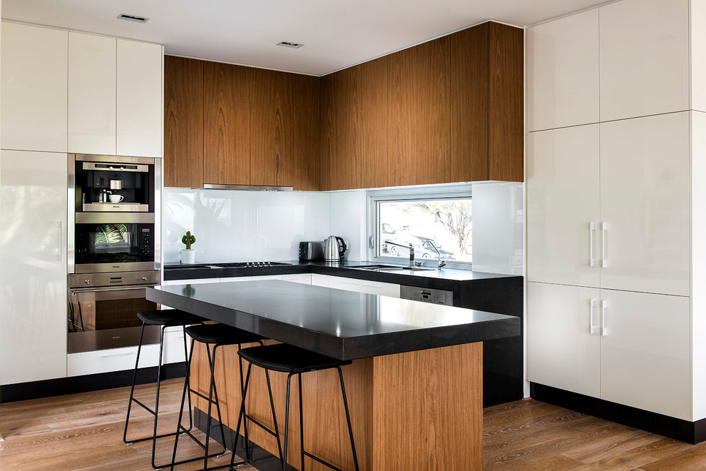 This is an example of a midcentury l-shaped kitchen in Perth with flat-panel cabinets, medium wood cabinets, white splashback, glass sheet splashback, medium hardwood floors and with island.