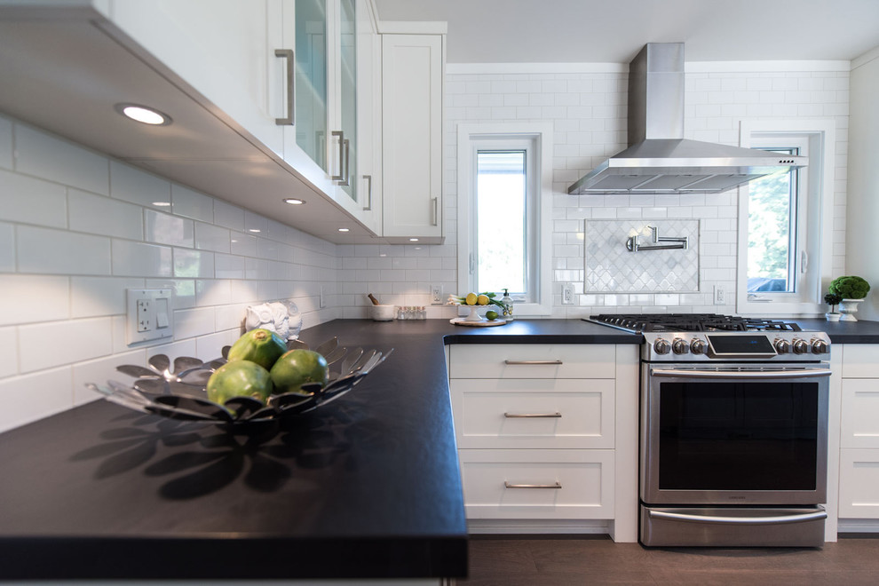 Example of a mid-sized classic l-shaped medium tone wood floor eat-in kitchen design in Vancouver with an undermount sink, shaker cabinets, white cabinets, solid surface countertops, white backsplash, subway tile backsplash, stainless steel appliances and an island