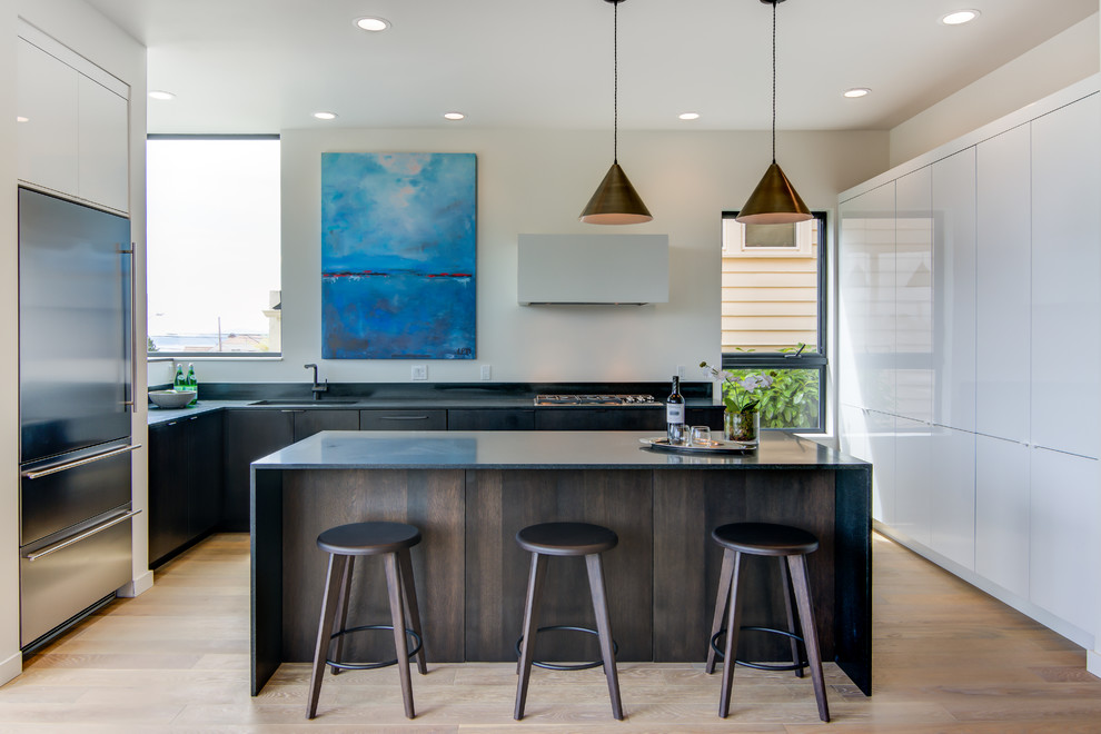 This is an example of a contemporary l-shaped kitchen in Seattle with flat-panel cabinets, dark wood cabinets, stainless steel appliances, light hardwood floors, with island, an undermount sink and white splashback.