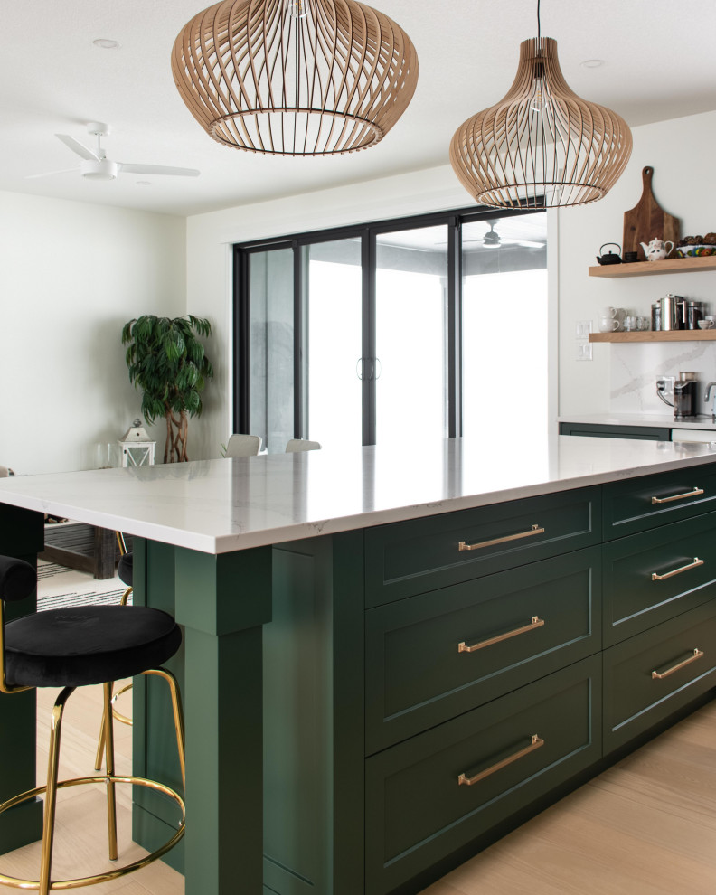 This is an example of a mid-sized country l-shaped open plan kitchen in Toronto with an undermount sink, shaker cabinets, green cabinets, quartz benchtops, white splashback, engineered quartz splashback, stainless steel appliances, light hardwood floors, with island, brown floor and white benchtop.