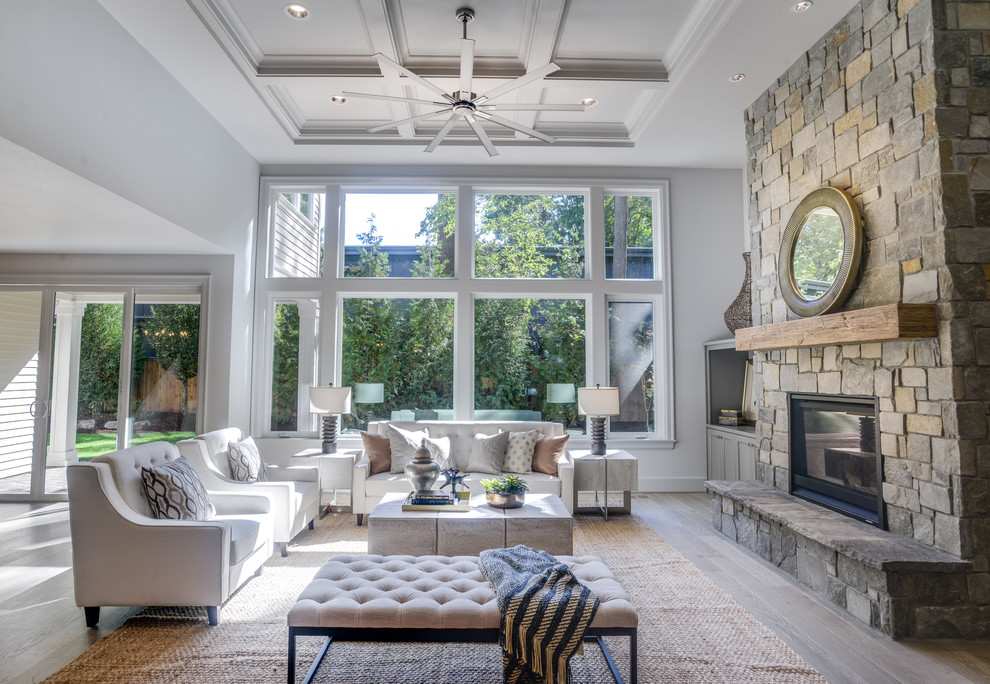 Photo of a transitional open concept living room in Portland with white walls, light hardwood floors, a standard fireplace, a stone fireplace surround and grey floor.