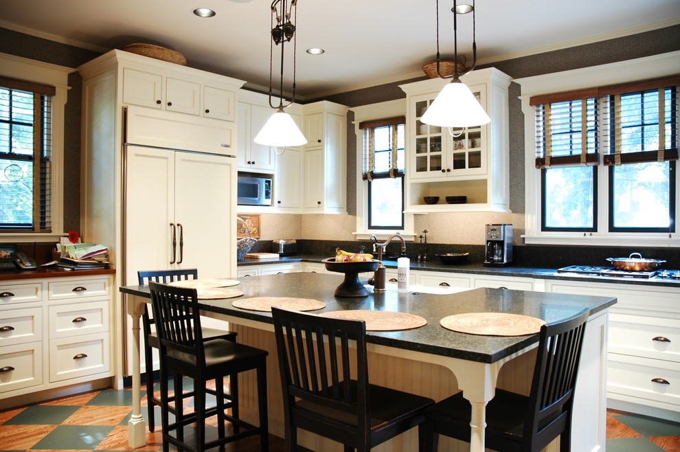 This is an example of a large traditional u-shaped eat-in kitchen in Chicago with a farmhouse sink, beaded inset cabinets, white cabinets, soapstone benchtops, panelled appliances, black splashback, stone slab splashback, light hardwood floors and with island.
