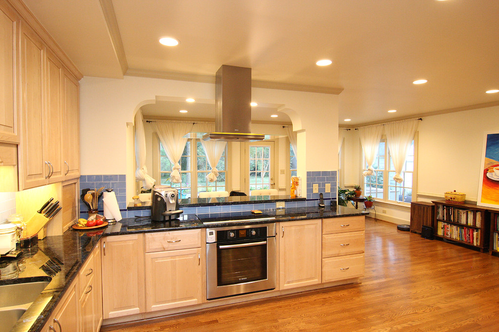 Huge transitional l-shaped medium tone wood floor open concept kitchen photo with an undermount sink, raised-panel cabinets, light wood cabinets, granite countertops, blue backsplash, glass tile backsplash and stainless steel appliances