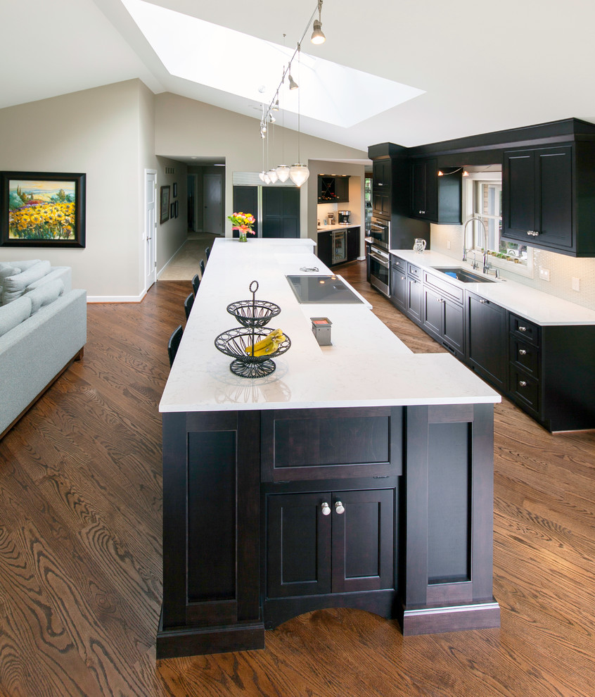 Large arts and crafts galley eat-in kitchen in Detroit with an undermount sink, beaded inset cabinets, dark wood cabinets, glass benchtops, beige splashback, ceramic splashback, stainless steel appliances, medium hardwood floors and with island.