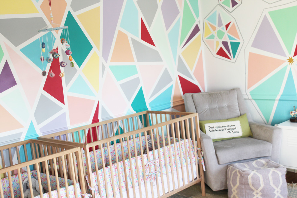 Photo of a small modern nursery for girls in Los Angeles with multi-coloured walls and dark hardwood floors.