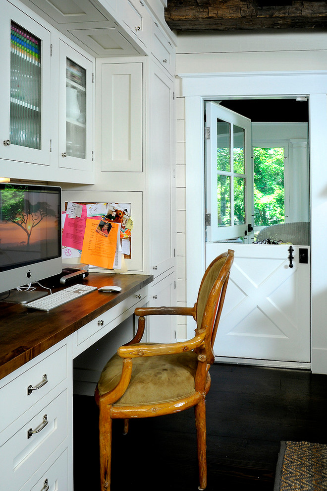 This is an example of a country home office in New York with white walls, dark hardwood floors and a built-in desk.