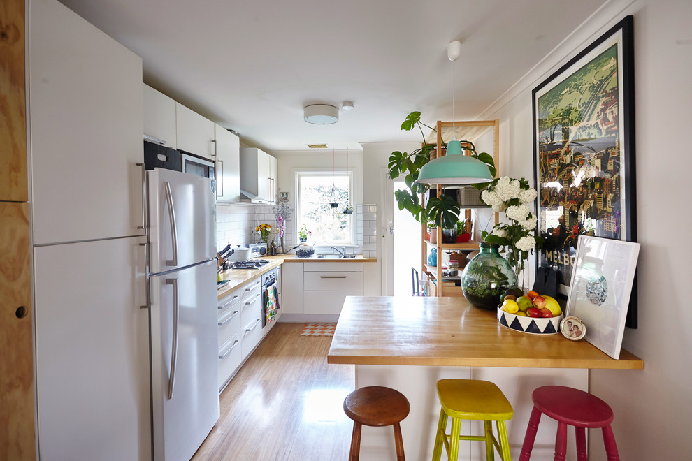 Inspiration for an eclectic kitchen in Melbourne with flat-panel cabinets, white cabinets, wood benchtops, white splashback, subway tile splashback, white appliances and medium hardwood floors.