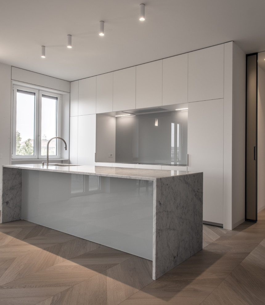 Expansive modern open plan kitchen in Milan with an undermount sink, flat-panel cabinets, white cabinets, marble benchtops, grey splashback, glass sheet splashback, stainless steel appliances and with island.