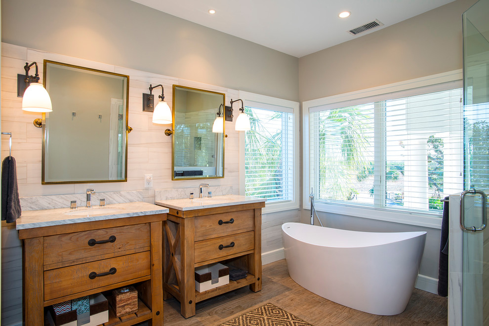 Photo of a mid-sized transitional master bathroom in Charleston with medium wood cabinets, a freestanding tub, a corner shower, beige tile, ceramic tile, ceramic floors, an undermount sink, marble benchtops, flat-panel cabinets, grey walls, brown floor and a hinged shower door.