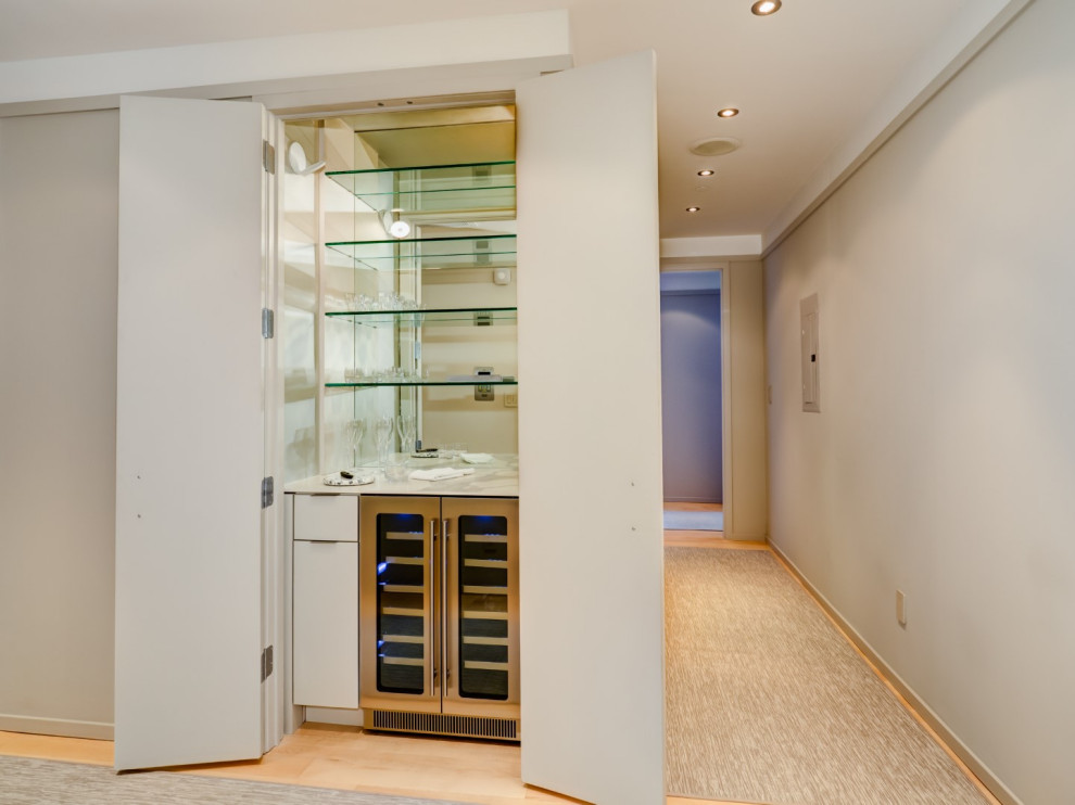 This is an example of a small contemporary single-wall home bar in New York with no sink, flat-panel cabinets, grey cabinets, tile benchtops, mirror splashback, light hardwood floors, yellow floor and grey benchtop.