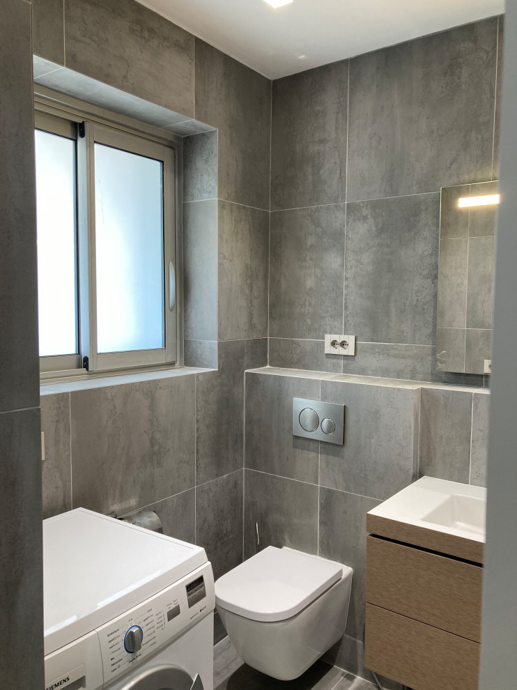 Idée de décoration pour un WC suspendu design de taille moyenne avec un carrelage gris, un mur gris, un plan vasque et un sol gris.