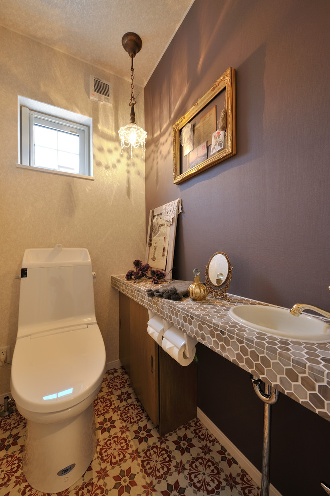 Photo of an eclectic powder room in Sapporo with flat-panel cabinets, medium wood cabinets, gray tile, brown tile, beige tile, purple walls, a drop-in sink and a two-piece toilet.