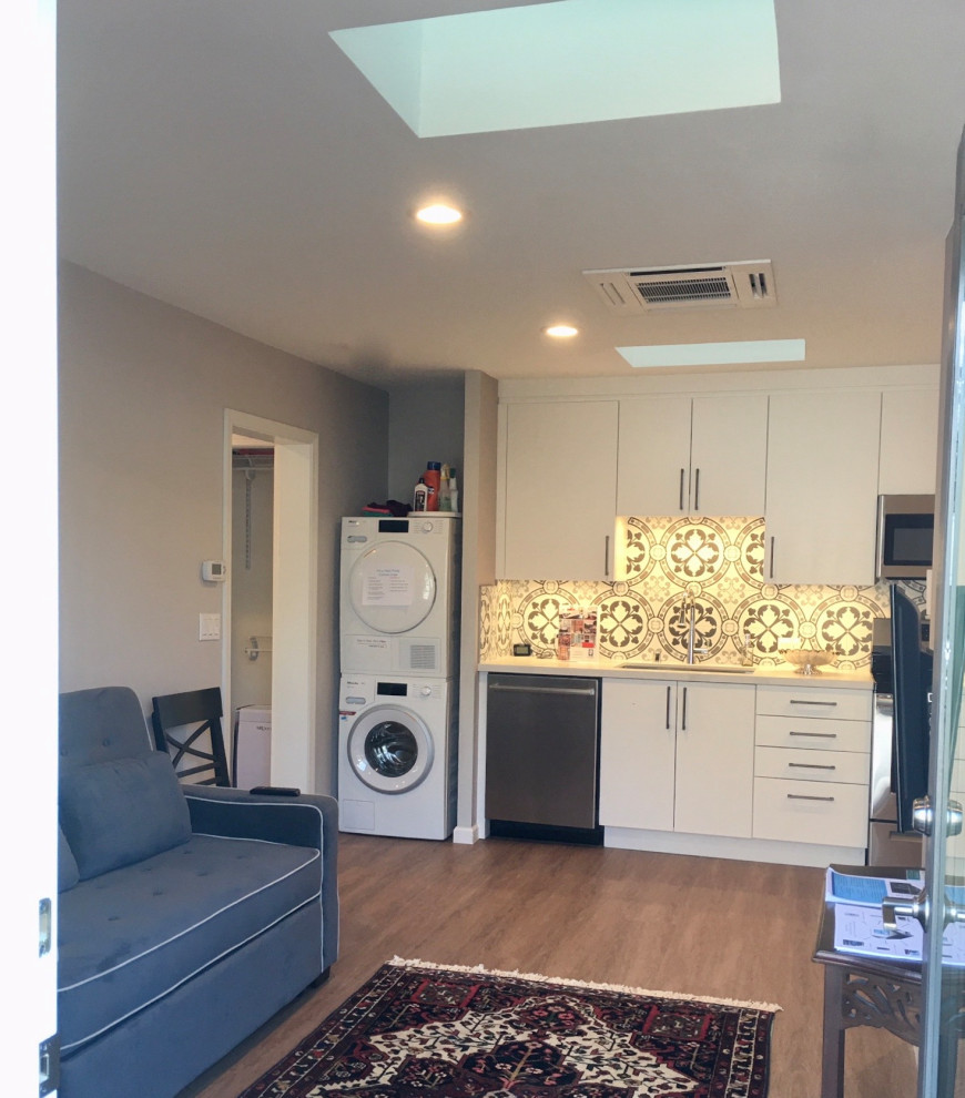 This is an example of a small transitional single-wall utility room in San Francisco with flat-panel cabinets, white cabinets, quartz benchtops, grey splashback, porcelain splashback, grey walls, vinyl floors, a stacked washer and dryer, brown floor and yellow benchtop.