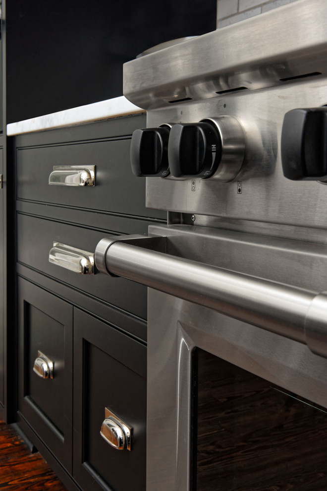Large transitional l-shaped medium tone wood floor and brown floor eat-in kitchen photo in DC Metro with a farmhouse sink, beaded inset cabinets, black cabinets, white backsplash, subway tile backsplash, stainless steel appliances, an island and quartzite countertops