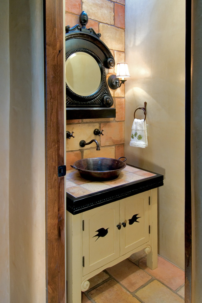 Inspiration for a small mediterranean powder room in Albuquerque with a vessel sink, furniture-like cabinets, yellow cabinets, tile benchtops, orange tile, terra-cotta tile, beige walls and terra-cotta floors.