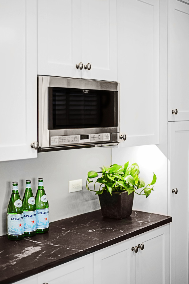 Eat-in kitchen - mid-sized transitional u-shaped medium tone wood floor eat-in kitchen idea with a farmhouse sink, shaker cabinets, white cabinets, onyx countertops, gray backsplash, subway tile backsplash, stainless steel appliances and an island