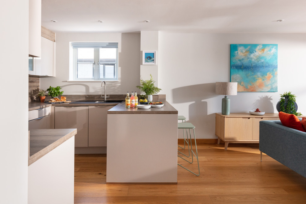 Inspiration for a mid-sized beach style u-shaped open plan kitchen in Cornwall with a drop-in sink, flat-panel cabinets, white cabinets, laminate benchtops, brown splashback, ceramic splashback, panelled appliances, medium hardwood floors, a peninsula, orange floor and brown benchtop.