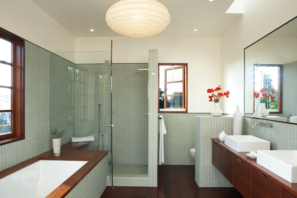 Inspiration for a contemporary master bathroom in Los Angeles with a vessel sink, flat-panel cabinets, medium wood cabinets, an undermount tub, an alcove shower, green tile, glass tile, white walls and dark hardwood floors.