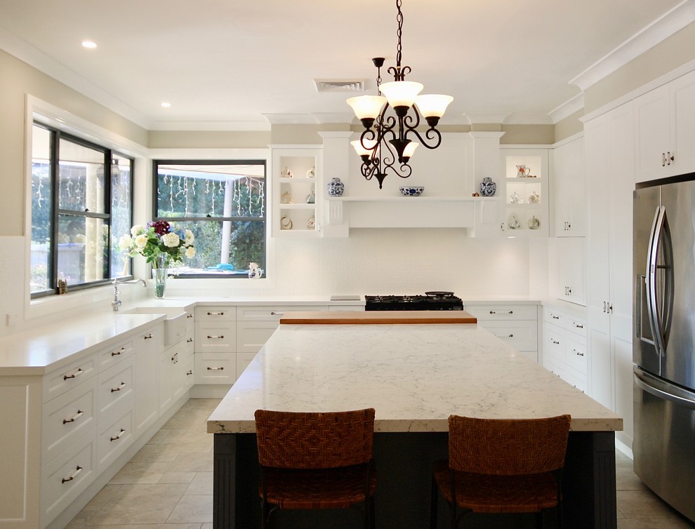 Design ideas for a mid-sized transitional u-shaped eat-in kitchen in Sydney with a farmhouse sink, shaker cabinets, white cabinets, quartz benchtops, white splashback, porcelain splashback, stainless steel appliances, porcelain floors, with island and beige floor.