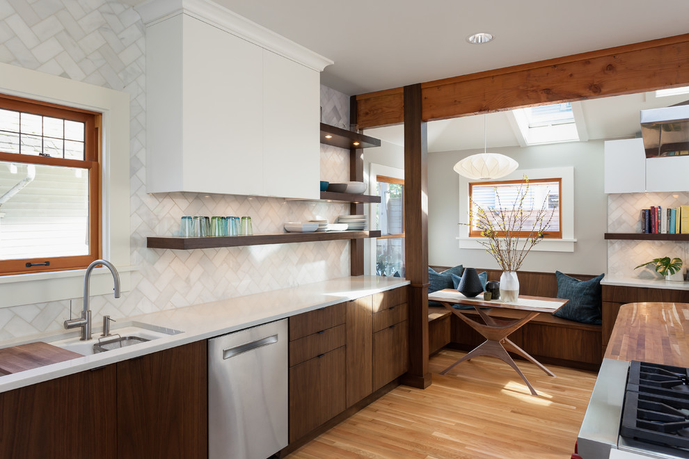 This is an example of a mid-sized midcentury l-shaped eat-in kitchen in Seattle with an undermount sink, flat-panel cabinets, medium wood cabinets, quartz benchtops, white splashback, stone tile splashback, stainless steel appliances, medium hardwood floors and a peninsula.