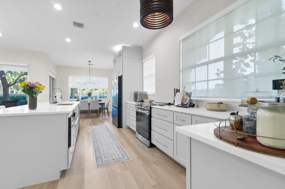 This is an example of a mid-sized scandinavian u-shaped eat-in kitchen in Miami with a drop-in sink, beaded inset cabinets, white cabinets, limestone benchtops, white splashback, stainless steel appliances, vinyl floors, with island, beige floor, white benchtop and vaulted.