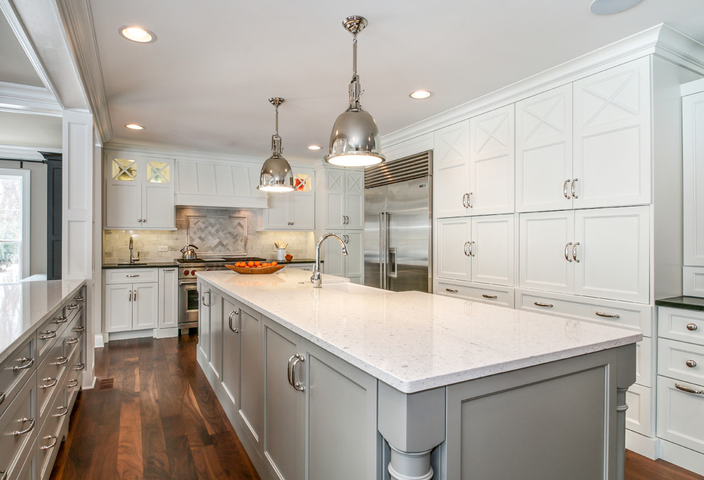This is an example of a large traditional u-shaped kitchen in Chicago with a farmhouse sink, shaker cabinets, white cabinets, white splashback, stainless steel appliances, dark hardwood floors, quartzite benchtops, with island and brown floor.