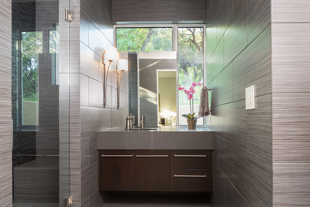 Photo of a mid-sized contemporary master bathroom in Austin with flat-panel cabinets, dark wood cabinets, an alcove shower, gray tile, stone slab, grey walls, ceramic floors, an integrated sink and solid surface benchtops.