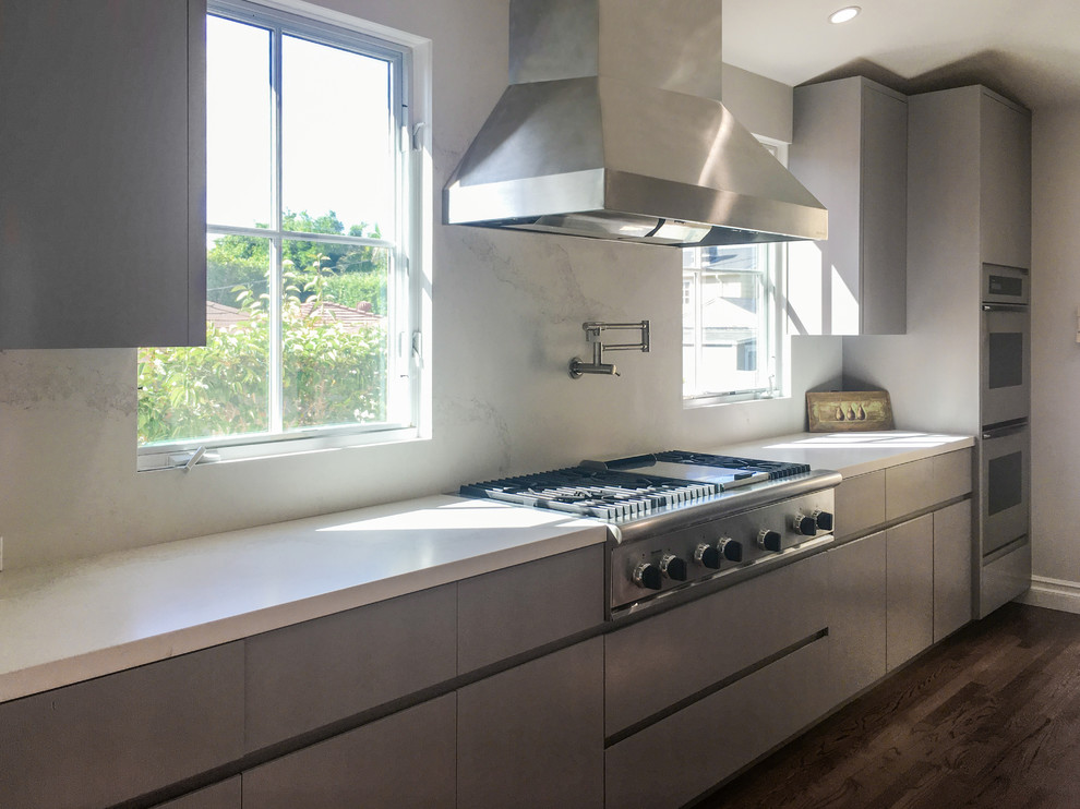 This is an example of a mid-sized modern galley separate kitchen in Los Angeles with flat-panel cabinets, grey cabinets, white splashback, stone slab splashback, stainless steel appliances, an undermount sink, solid surface benchtops, medium hardwood floors and with island.