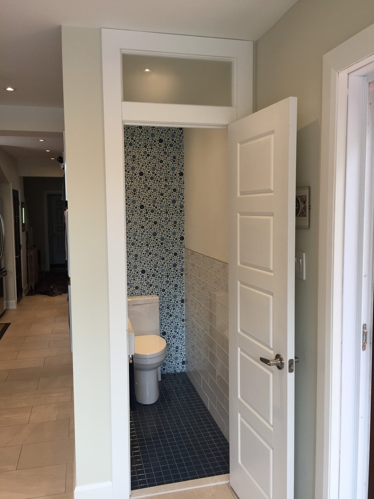 Small transitional powder room in Montreal with a one-piece toilet, blue tile, porcelain tile, white walls, porcelain floors and a wall-mount sink.