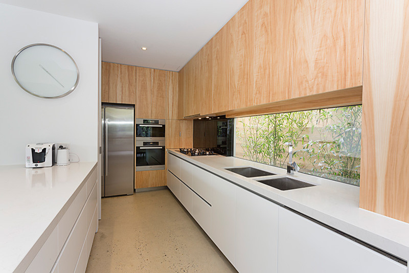 Large contemporary u-shaped eat-in kitchen in Other with a double-bowl sink, flat-panel cabinets, white cabinets, glass sheet splashback, stainless steel appliances, concrete floors, with island and white benchtop.