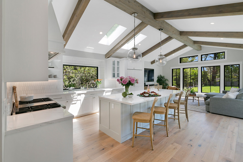 Large traditional l-shaped open plan kitchen in San Francisco with a submerged sink, shaker cabinets, white cabinets, engineered stone countertops, white splashback, porcelain splashback, stainless steel appliances, light hardwood flooring, an island, beige floors, white worktops and exposed beams.