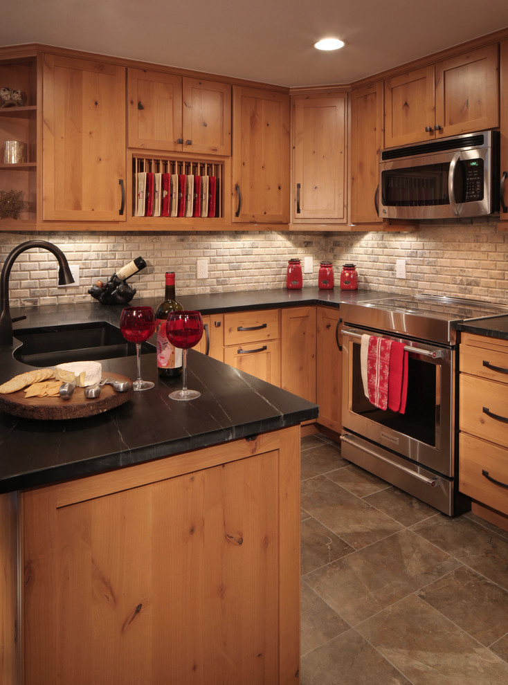 Example of a mountain style u-shaped porcelain tile eat-in kitchen design in Denver with an undermount sink, shaker cabinets, soapstone countertops, beige backsplash, stone tile backsplash and stainless steel appliances