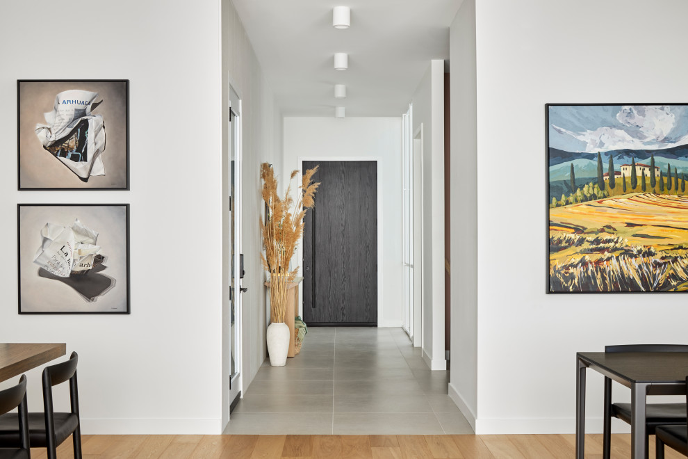 На фото: узкий коридор в скандинавском стиле с белыми стенами, полом из керамической плитки и серым полом с