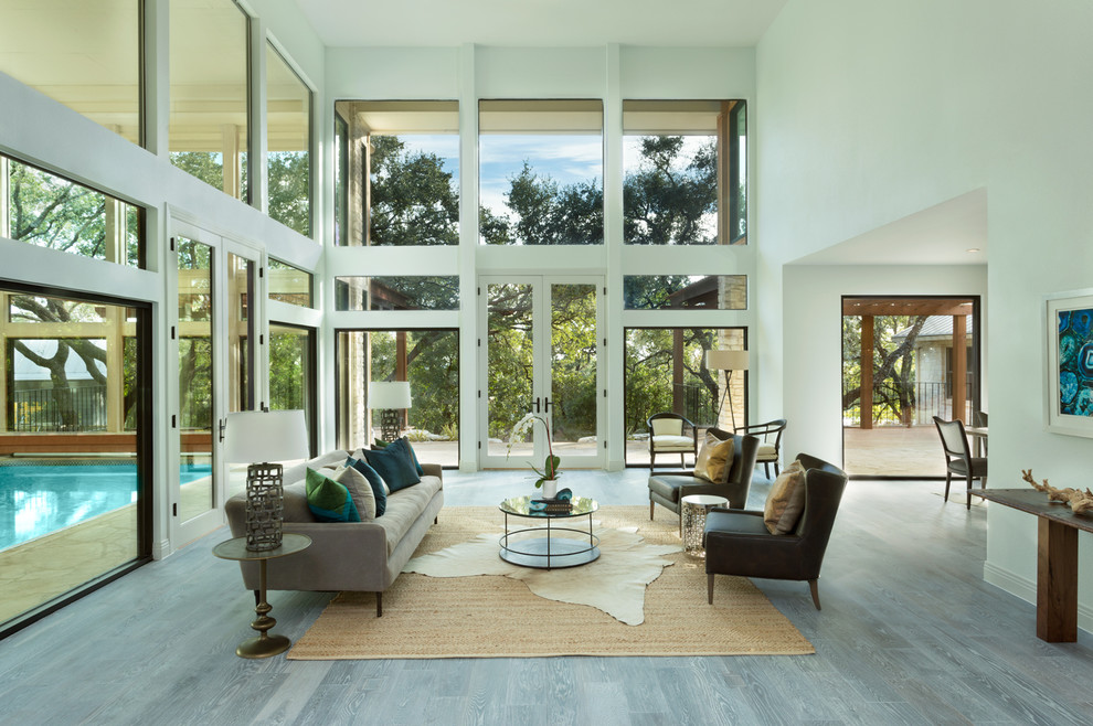 This is an example of an expansive contemporary formal open concept living room in Austin with light hardwood floors, white walls and a concealed tv.
